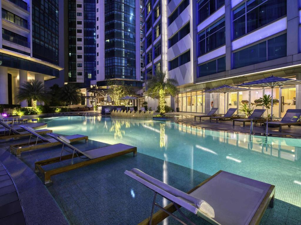 An illuminated outdoor pool surrounded by loungers and tall hotel buildings.