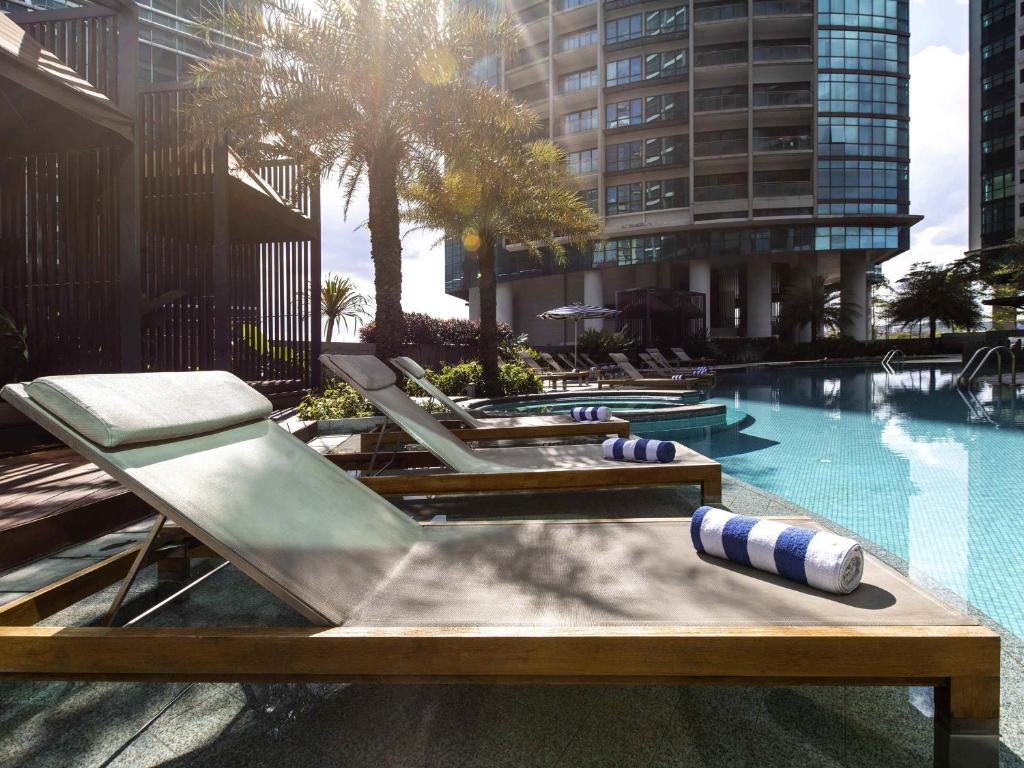 A sunny pool deck with cushioned loungers beside an outdoor swimming pool.