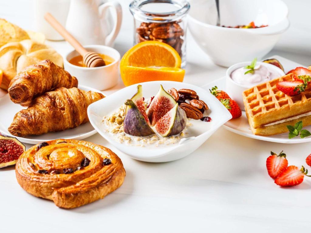 A bright breakfast spread featuring pastries, fruit, yoghurt, cereal and waffles.