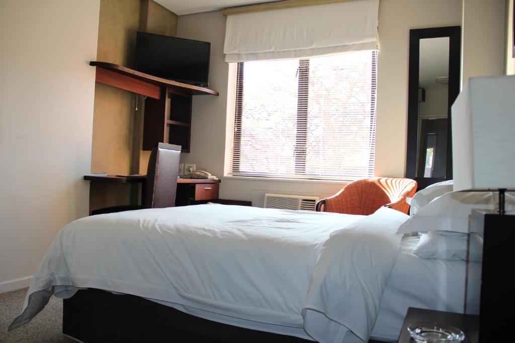 um quarto com uma cama branca e uma janela em Illovo Hotel em Joanesburgo