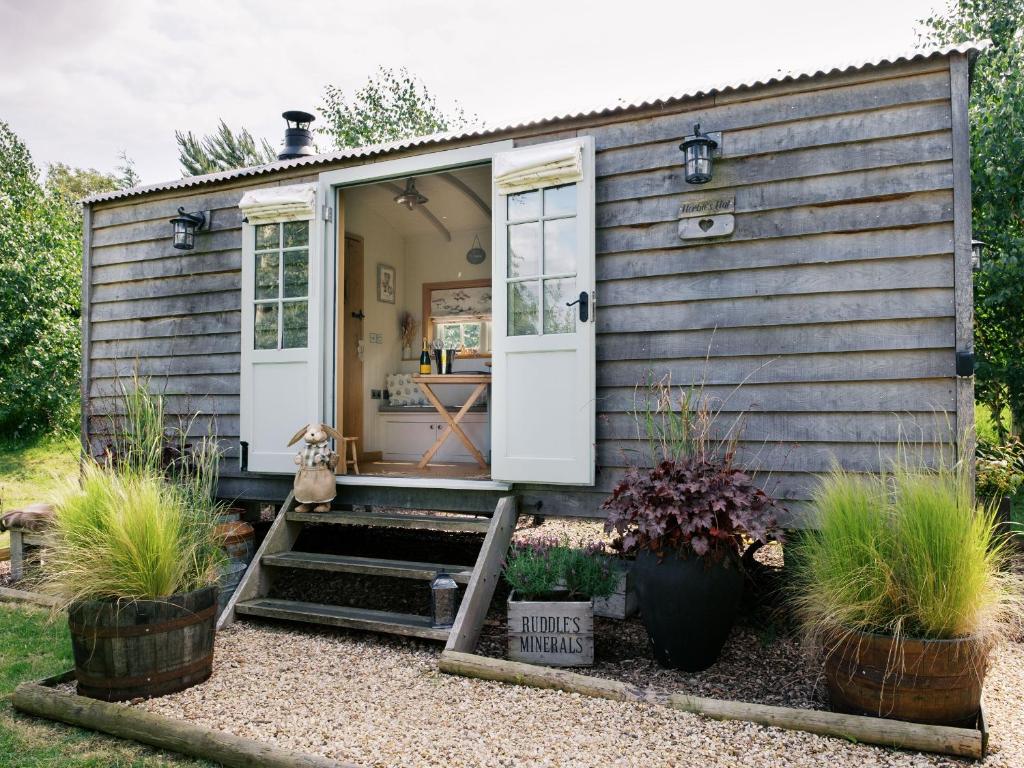 a tiny house with white doors and plants in a yard at Herbie's Shepherds Hut at Shepherds Lodge Retreat and Wellness in Nottingham
