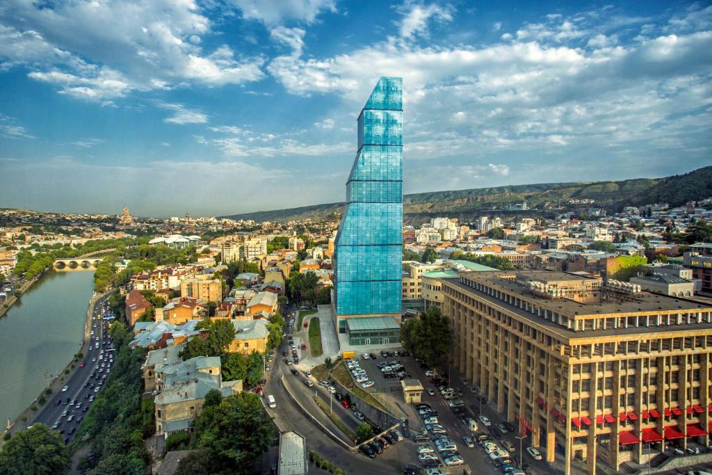 uma vista para uma cidade com um arranha-céus de vidro alto em The Biltmore Tbilisi Hotel em Tbilisi