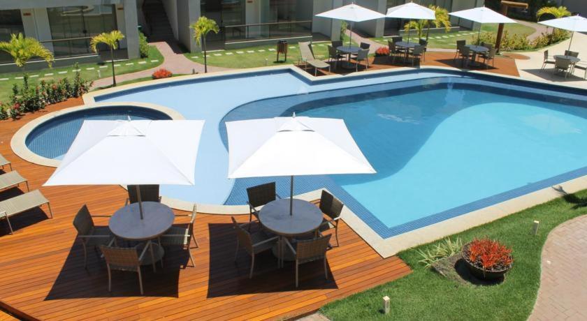 a large swimming pool with tables and umbrellas on a deck at Imbassaí Solaris Village 2 quartos in Imbassai