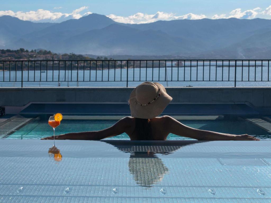 a woman sitting in a swimming pool with a wine glass at ibis Styles Ajaccio Napoleon in Ajaccio