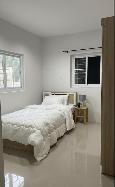 a white bedroom with a large bed and two windows at Phimpakan guesthouse in Nakhon Phanom