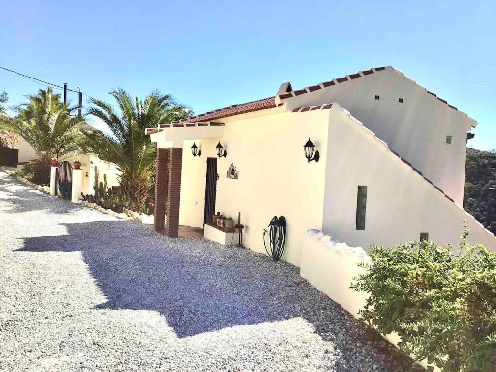 a white house on a gravel road with palm trees at Cortijo Chupito in Yunquera