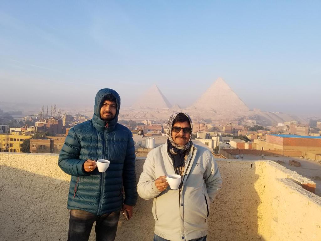 two men holding coffee cups in front of the pyramids at Hany pyramids view in Cairo