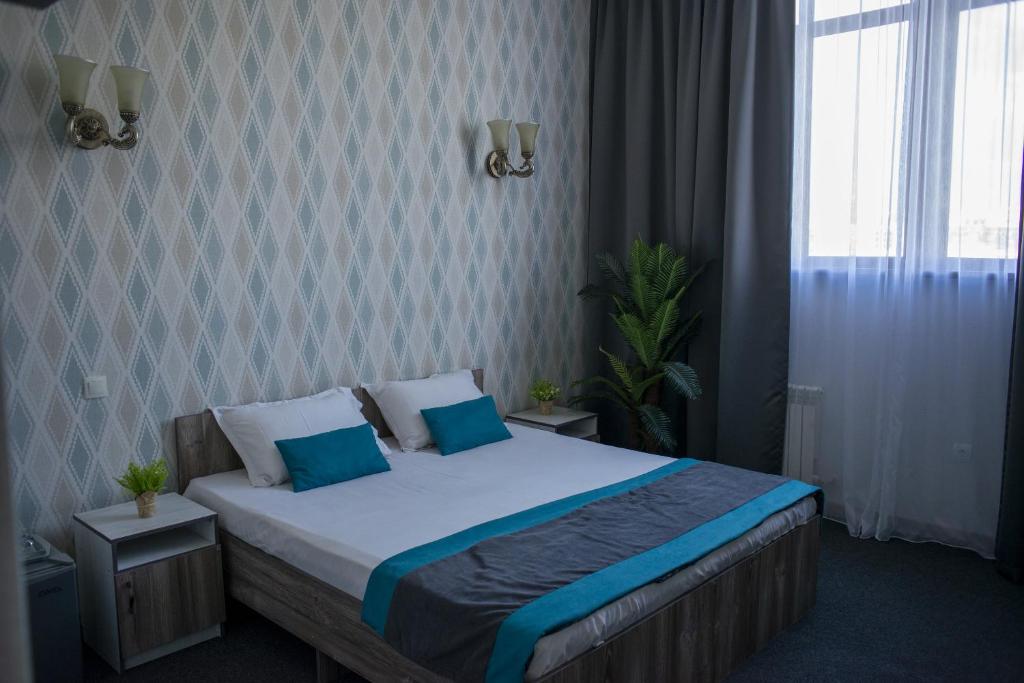 a bedroom with a bed with blue pillows and a window at Tarlan Hotel in Aktau