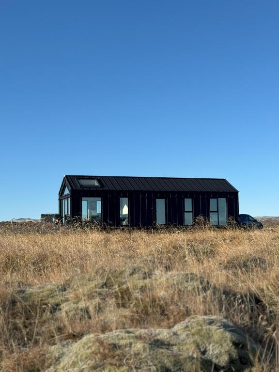 a black house in the middle of a field at LL Properties - Aurora Lodges in Grímsnes og Grafningshreppur