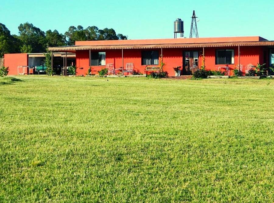 a red house with a large field in front of it at FincaMora in Colonia del Sacramento