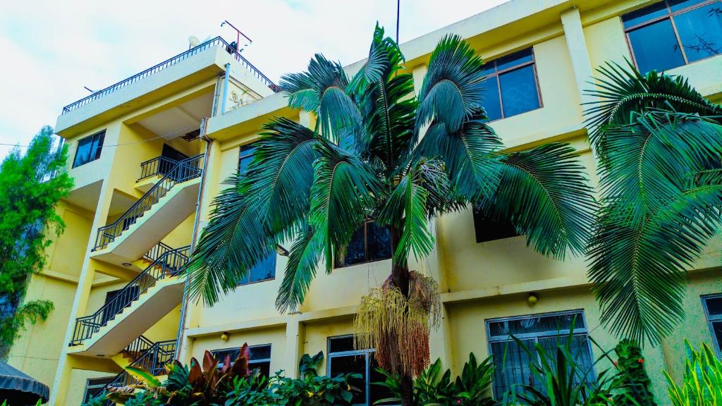 a yellow building with a palm tree in front of it at Arusha Diplomat Hotel & Conference in Marombosa