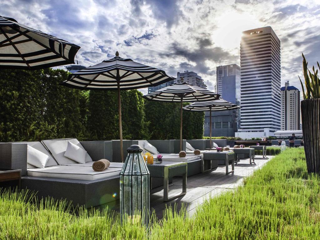 a rooftop patio with umbrellas and couches and tables at Mövenpick Hotel Sukhumvit 15 Bangkok in Bangkok