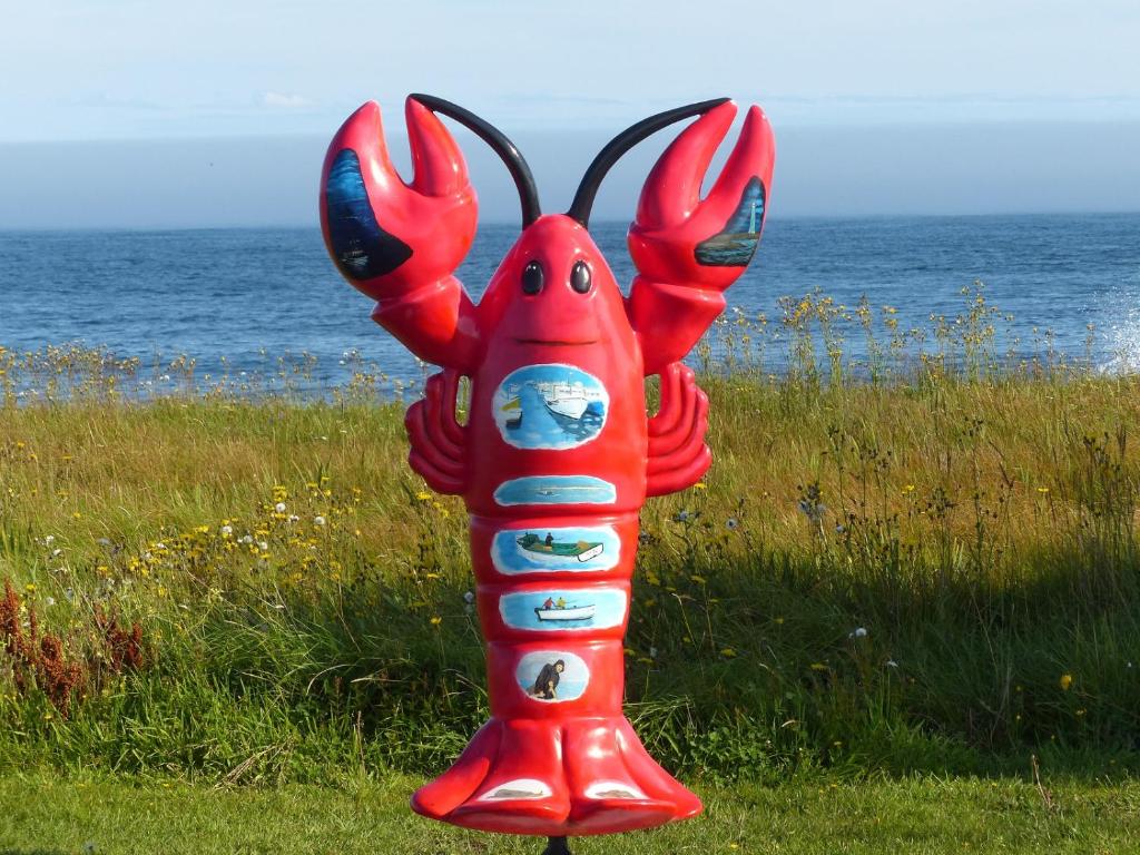 a red statue of a lobster in the grass near the ocean at Route3BnB in Shag Harbour