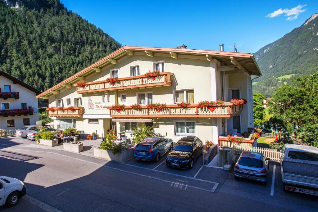 un gran edificio con coches estacionados en un estacionamiento en Pension St.Lukas, en Pfunds