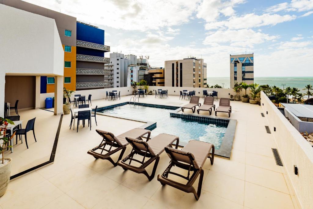 a rooftop patio with a swimming pool and chairs and tables at El Aram Beach Express in Maceió
