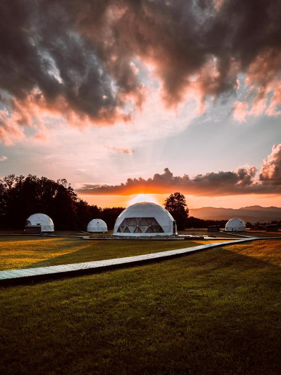 a group of domes in a field with a sunset at Glamping Resort in Dolný Kamenec