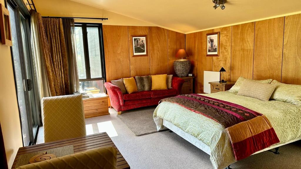 Hawkshead Boutique Studio & Gardens في ماكارورا: غرفة نوم بها سرير وكرسي أحمر