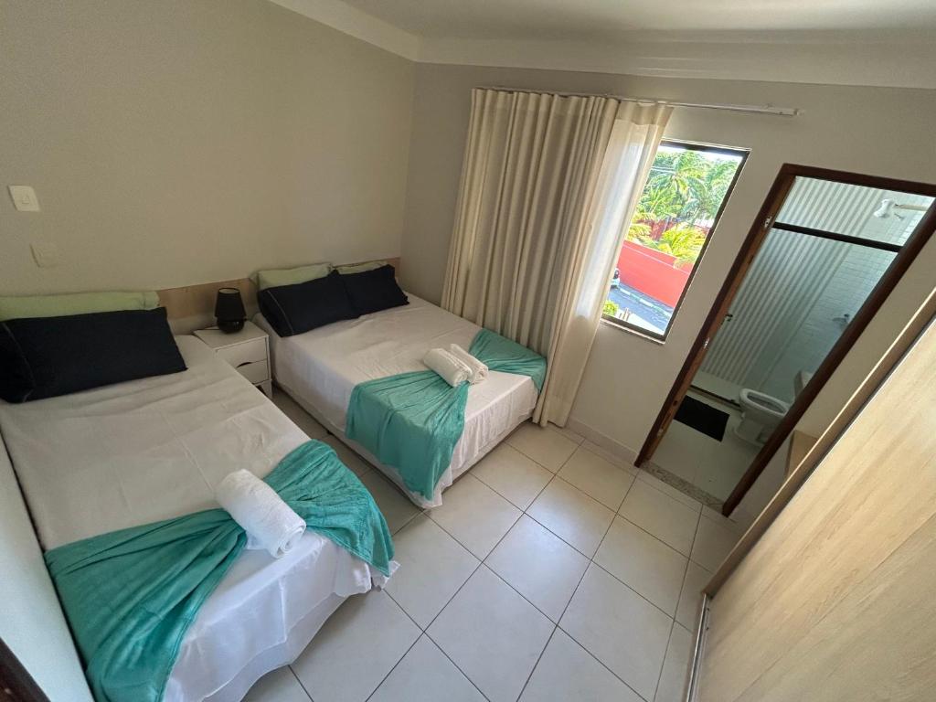 two beds in a hotel room with a window at Village duplex Guarajuba 3 suítes in Camacari
