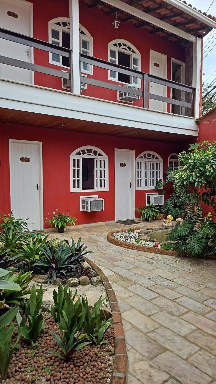 a red house with white windows and a patio at Guest House Flor de Laranjeira in São Pedro da Aldeia