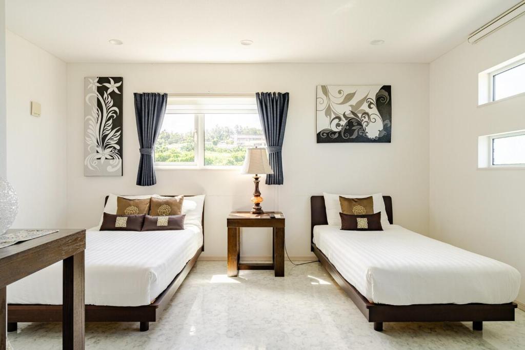 a bedroom with two beds and a table and a window at Casa de nicki 恩納村 in Onna