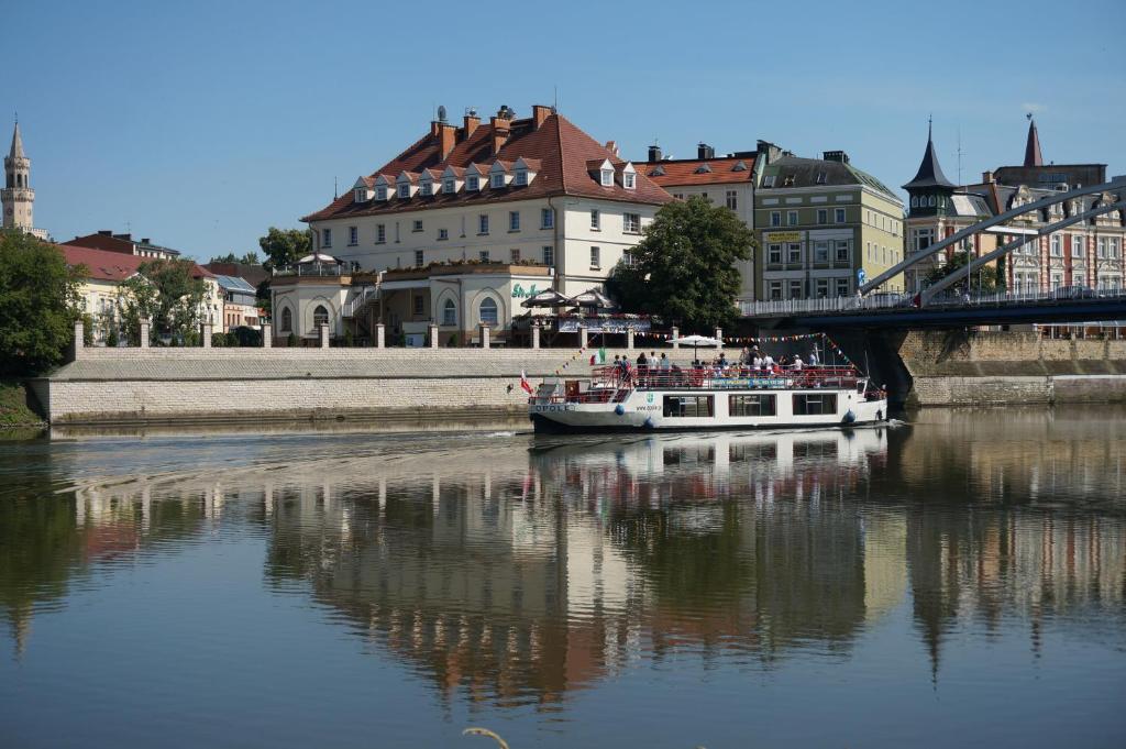 een boot op een rivier met gebouwen en een brug bij Hotel Piast in Opole