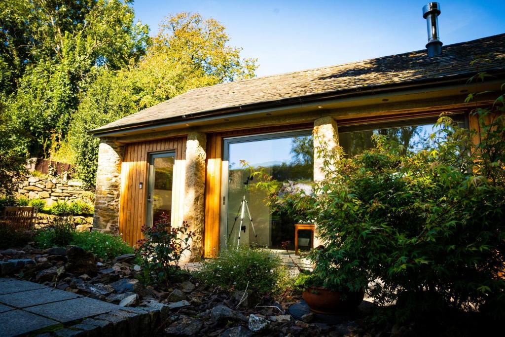 a house with large glass windows in a garden at Cosy Rural Barn with Private Garden & Forest - The Cart Barn in Tavistock