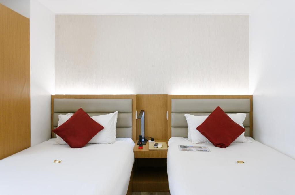 two beds in a hotel room with red pillows at LivStudios Manila Bay in Manila