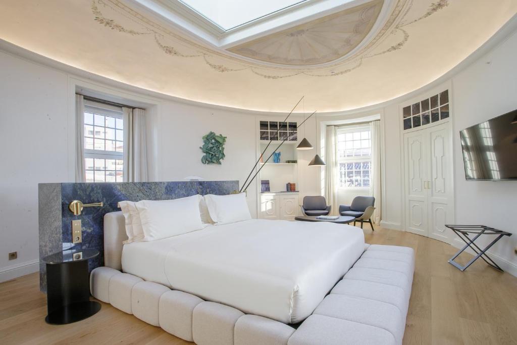 A bright guest room pairs a large upholstered bed with a sitting area and period architectural details.