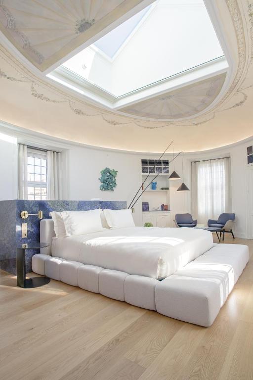 A spacious white guest room features a large upholstered bed, skylight and separate lounge chairs.