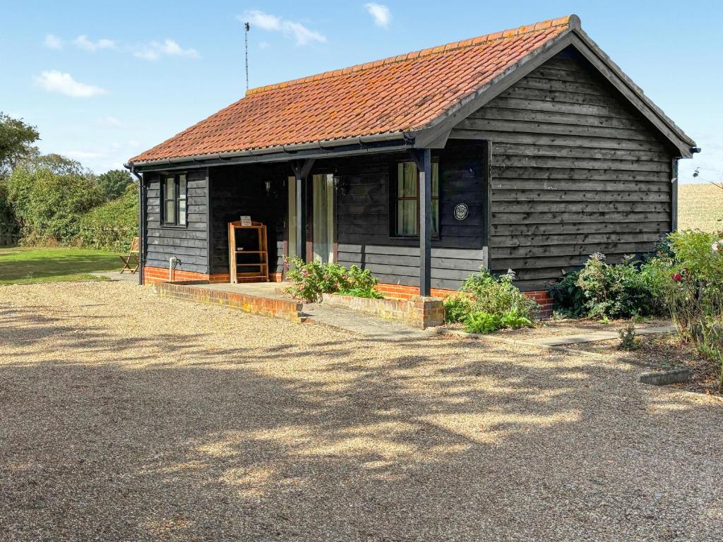 a small black house with a porch and a driveway at Fuschia Chalet in Framlingham