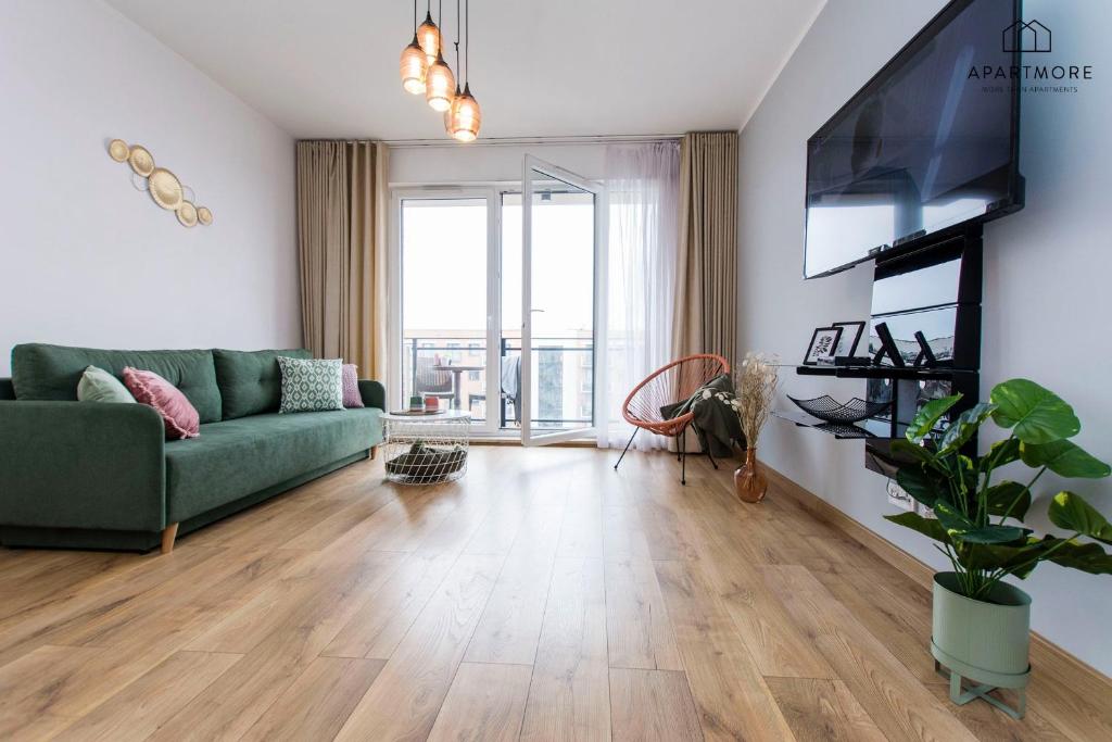 Bright living room with green sofa, wall-mounted TV, open balcony doors and potted plant.
