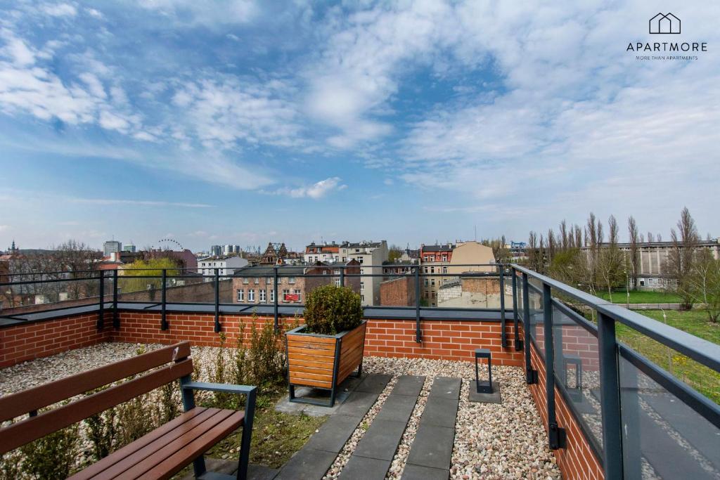 Rooftop terrace with wooden bench, planter boxes, pebble path and glass railing overlooking city.