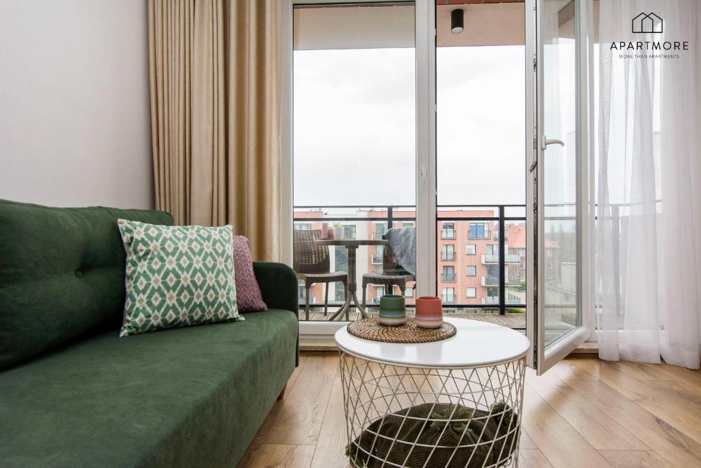 Green sofa beside open balcony doors, round coffee table with decor, outdoor seating visible
