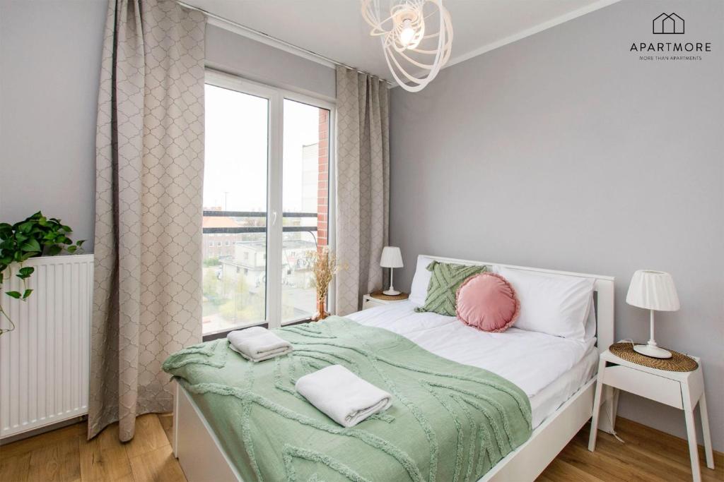 Sunny bedroom with double bed, green textured throw, pink round cushion and bedside lamps.