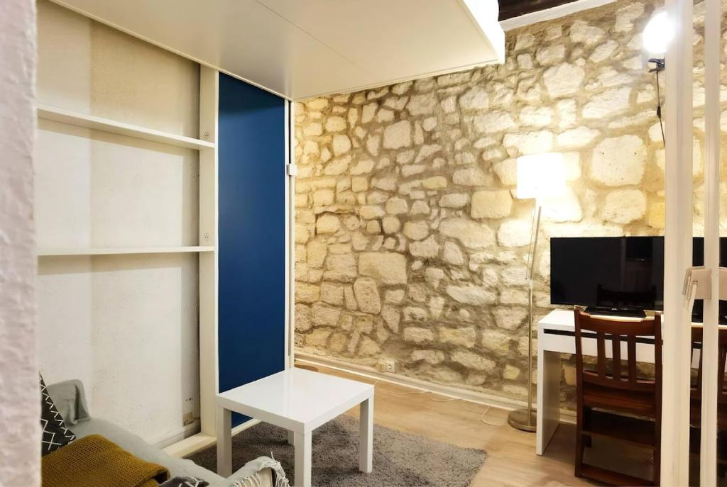 a room with a stone wall with a desk and a tv at Cute Marais Studio near Metro Heart of Paris N4-22 in Paris