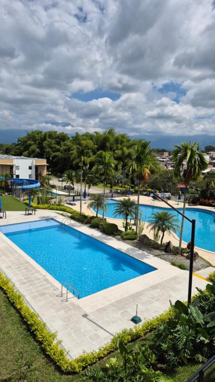 a large swimming pool with palm trees in the background at CASA Y APARTAMENTOS PRIVADOS 2 y 3 habitaciones, PISCINA, JACUZZY, SAUNA cerca Aeropuerto, parque Del Cafe By Molca Xperiences in Armenia