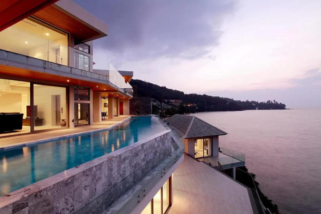 a house with a swimming pool next to the water at Cape Sienna Villa 4-Oceanfront 5-Bedroom Luxury Villa with 22 m Infinity Pool in Kamala Beach