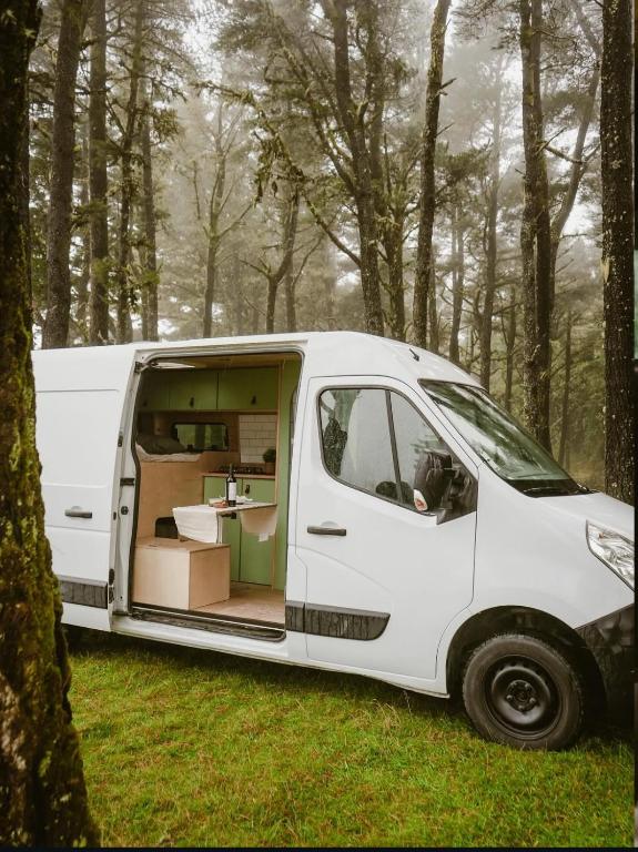 Una furgoneta blanca aparcada en el bosque con la puerta abierta en Bawhee - Campervan, en Caniço