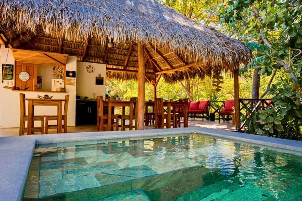 a resort with a swimming pool and a thatch hut at Antema Lodge Secteur Tamarindo, piscine, yoga, gym, jungle et paix in Tamarindo
