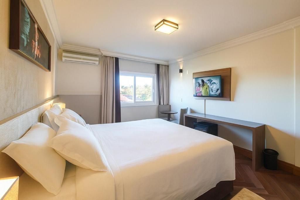 a hotel room with a large white bed and a desk at Suíte Confort - Resort no Coração de Gramado in Gramado