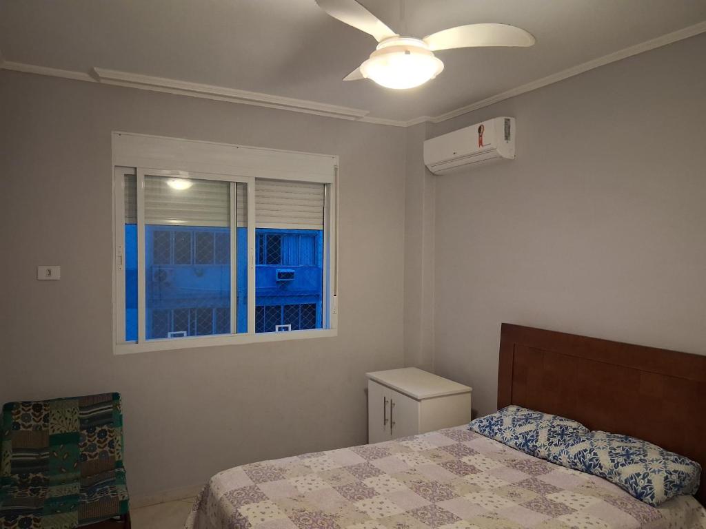 Un dormitorio con una cama con ventilador de techo y una ventana. en Quarto em frente a praia do Boqueirão, en Santos