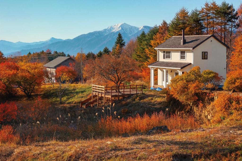 a white house on a hill with autumn foliage at 富士山が見える八ヶ岳南麓の家 in Nagasawa