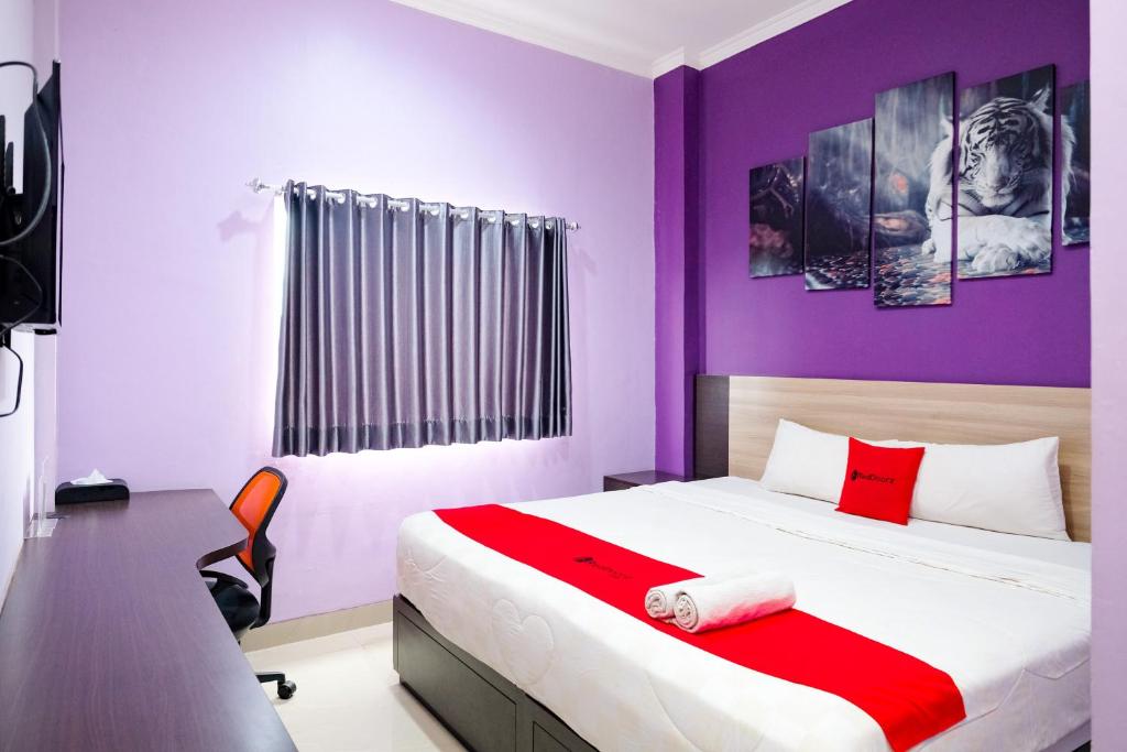 Schlafzimmer mit einem Bett mit lila Wänden und einem Schreibtisch in der Unterkunft RedDoorz @ myRoom UMY in Yogyakarta