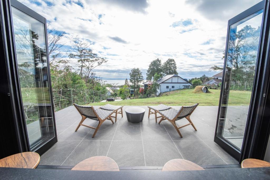 a patio with two chairs and a table and windows at Doggo伊豆　愛犬と過ごす最高の時間の為に造られた貸切宿。温泉、プライベートドッグランで最高の一時を。 in Ito