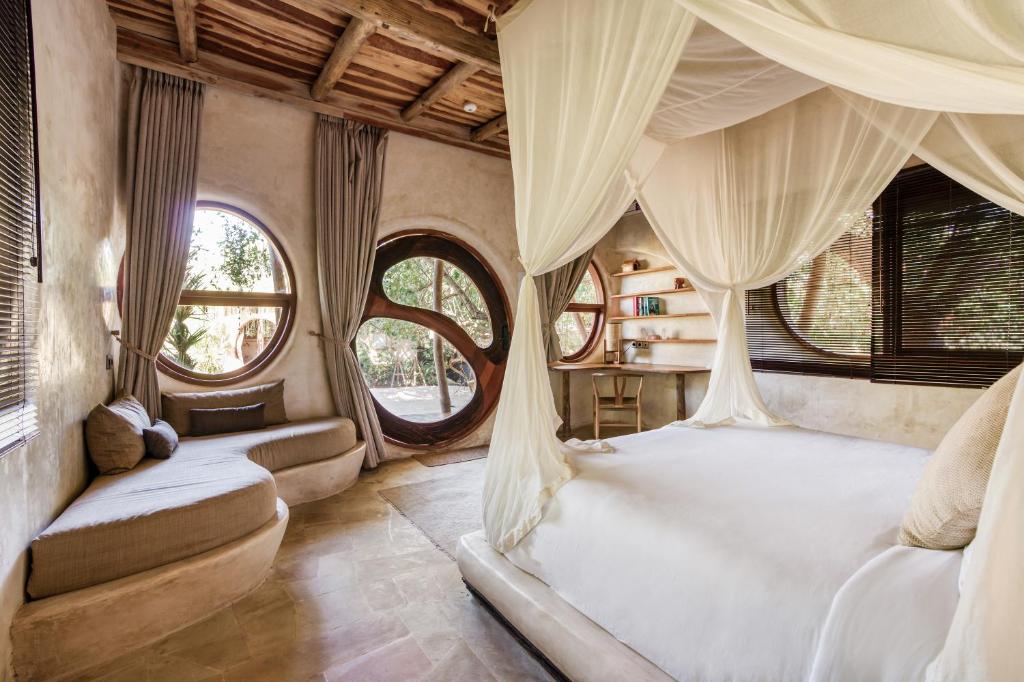 a bedroom with a bed with curtains and windows at Nuanu Suites & Accommodations in Tanah Lot