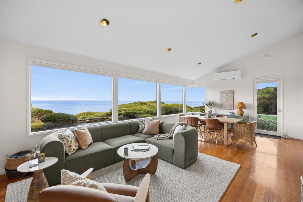 a living room with a couch and tables and windows at Heath Cliff House in Aireys Inlet