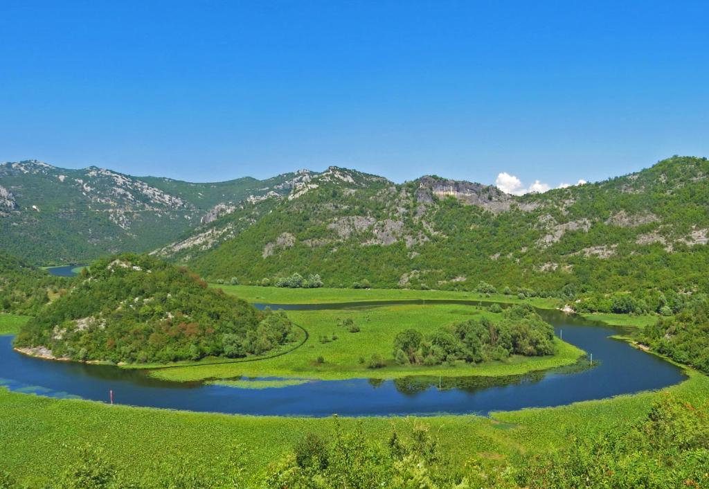 an island in a river with mountains in the background at Estate & Winery San Duyevo in Rijeka Crnojevića