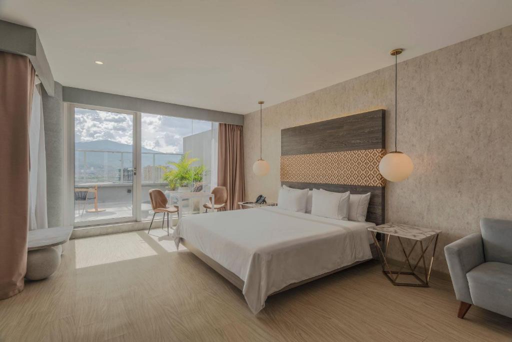 メデジンにあるV Grand Hotel, a member of Radisson Individualsのベッドとテーブルと椅子のあるホテルの部屋