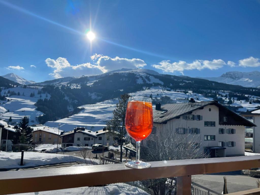 a glass of wine sitting on a balcony with a snow covered mountain at Savognin Rundigna in Savognin