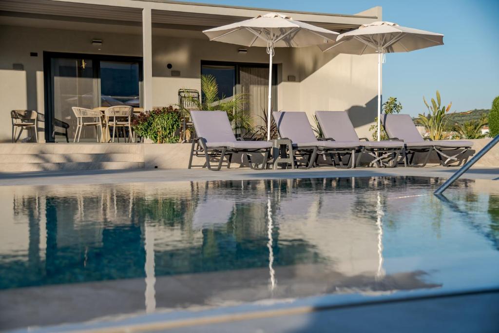 a pool with chairs and umbrellas next to a house at Villa La Caretta in Alikanas